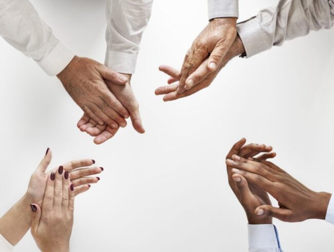 1803026 Three Cheers For Success overhead view of four pairs of hands in clapping position, white shirts shown on arms - image is cropped at wrists